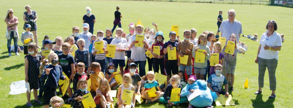 Viele Kinder auf einem Sportplatz, die ihre Urkunden und Gewinne zeigen
