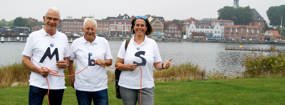 Zwei Männer und eine Frau stehen vor einem Stadtpanorama und halten ein Seil in der Hand