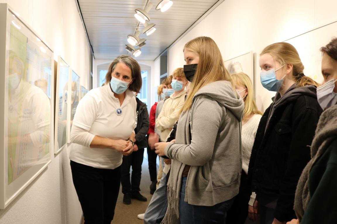 Schülerinnen und Schüler schauen sich gemeinsam mit einer Frau ein Bild an