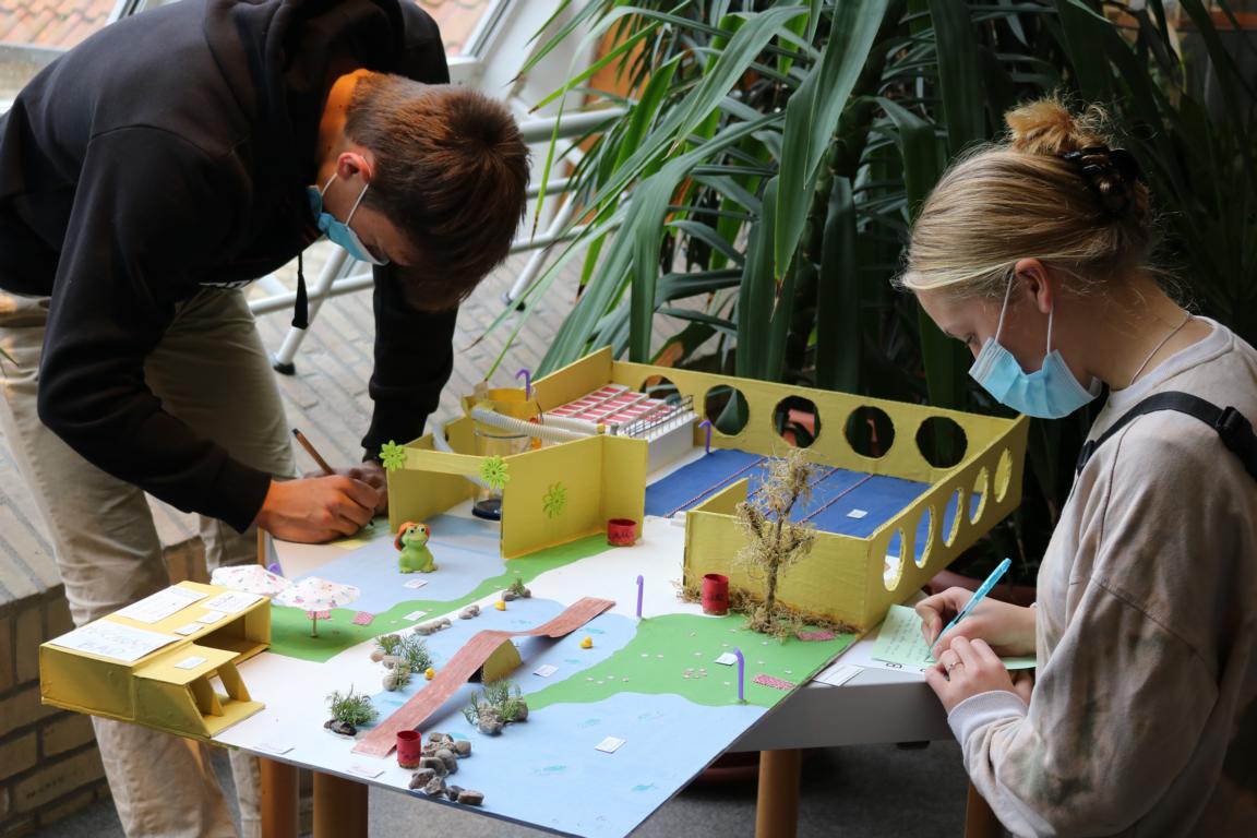 Ein Mädchen und ein Junge machen sich Notizen zu einem Schwimmhallenmodell.