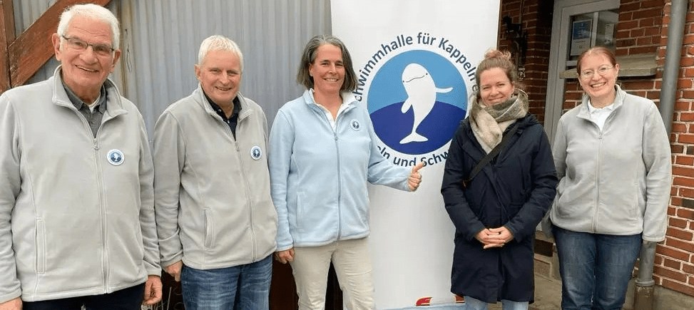 Zwei Männer und drei Frauen stehen vor einem Werbe-Roll-Up des Schwimmhallenvereins und lächeln in die Kamera